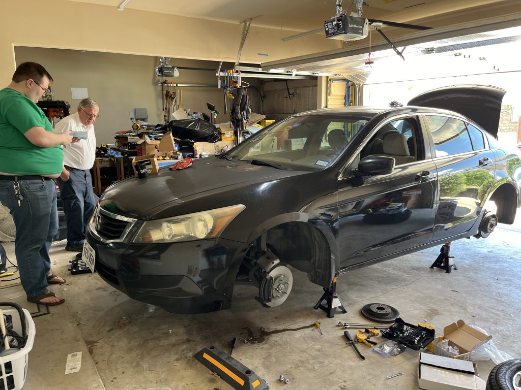 Learning is messy and dirty! My garage on June 22, 2024. Kyle (left) and Lance (on the floor behind the car) with their Grandpa Hellewell (white shirt) diagnosing another problem before heading to the auto parts store again.